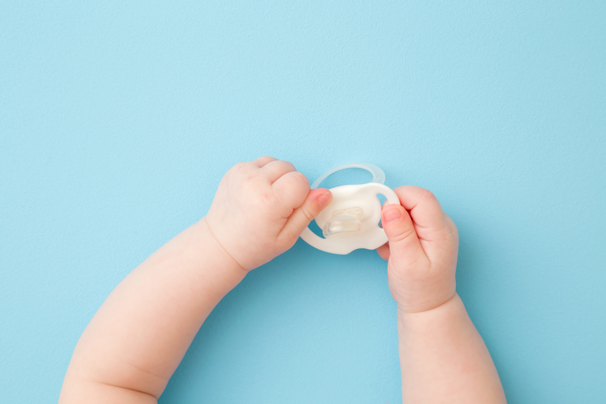 Image of a baby hands, holding a pacifier.