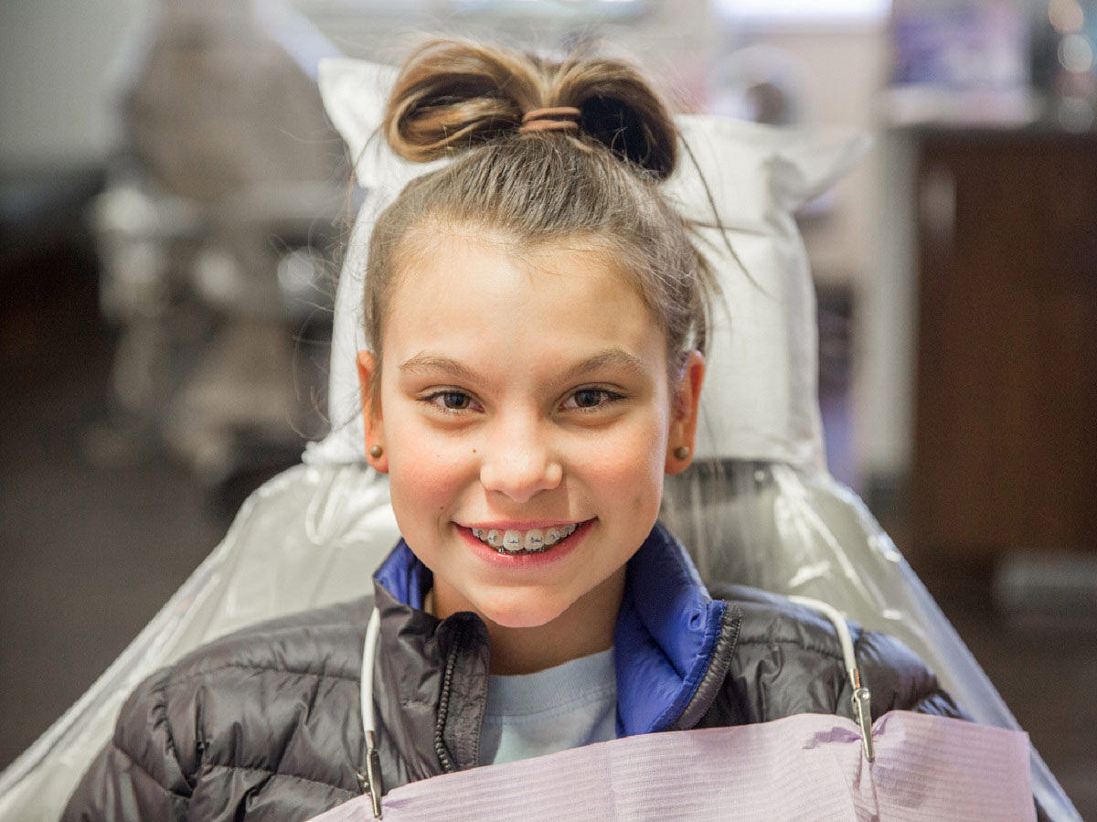 Young girl sitting in an orthodontic chair, smiling, and staring her treatment journey.