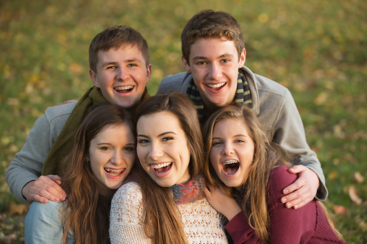 Group of teenage boys and girls smiling at the camera. Some have braces, while others have already completed orthodontic treatment.